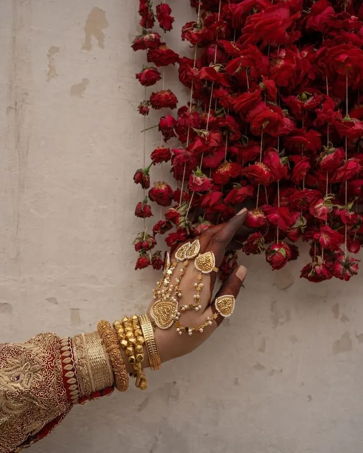 Gold hand jewellery and bangles in front of hanging red roses