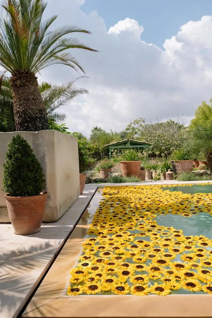 Swimming pool strewn with floating yellow sunflowers beside a palm and terracotta planters — yellow-themed decor