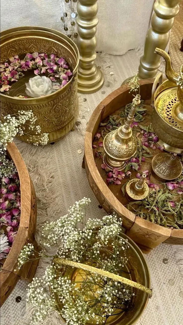 Ornate brass bowls and wooden trays of dried rose petals, baby's breath and attar holders on a cream textured cloth