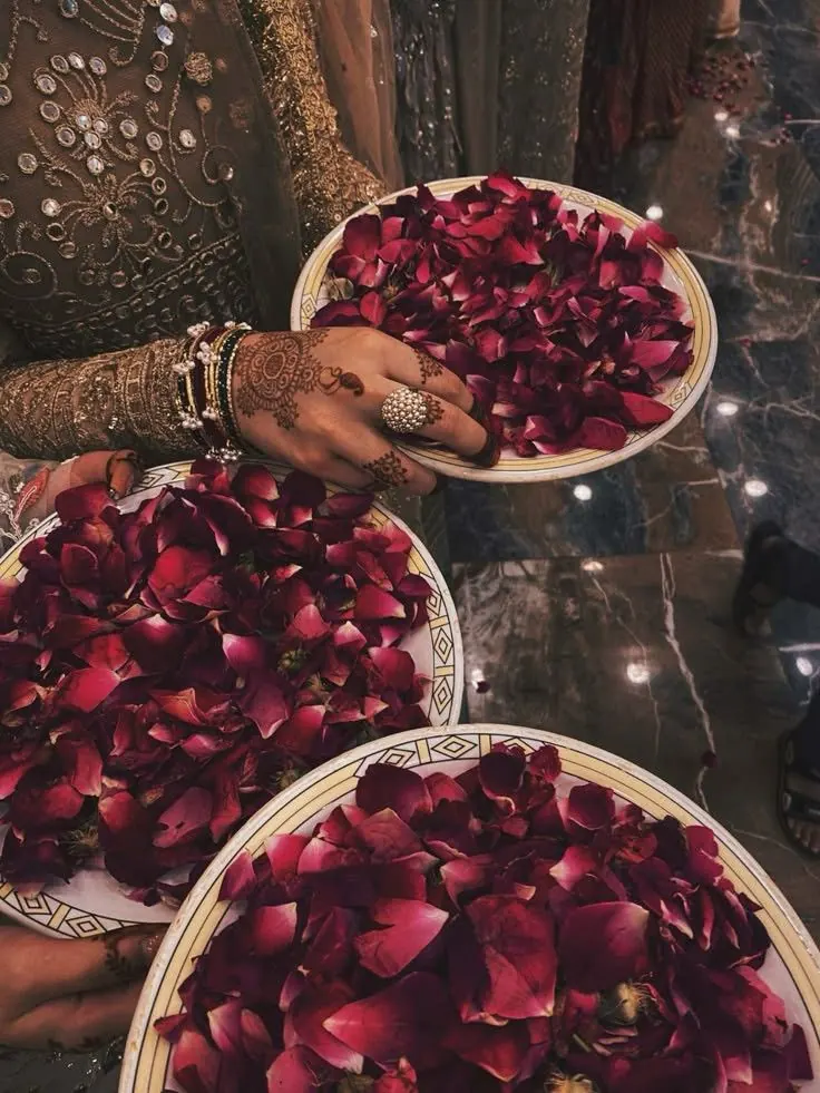 Henna-adorned hands holding brass plates filled with rose petals