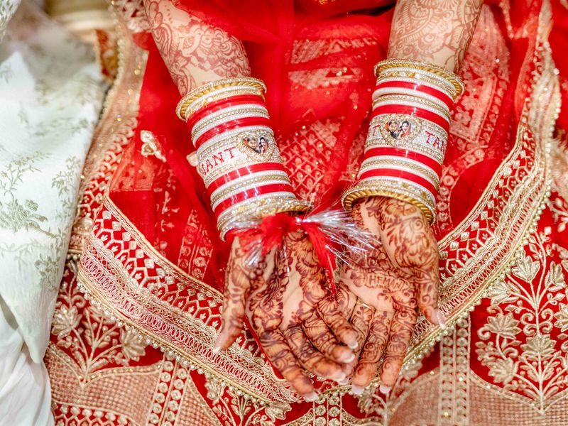 Bride's mehndi-covered hands wearing a red and white choora