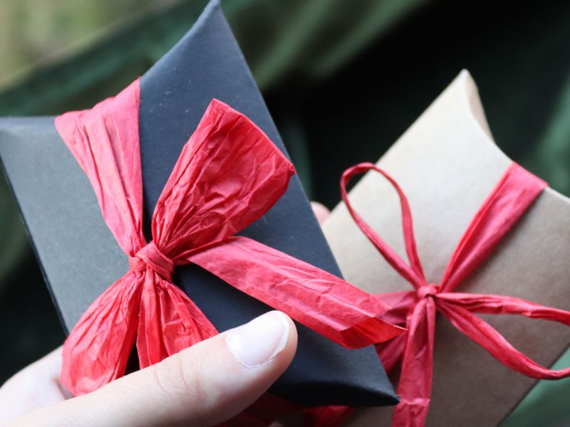 Hands holding small gift boxes tied with red ribbon