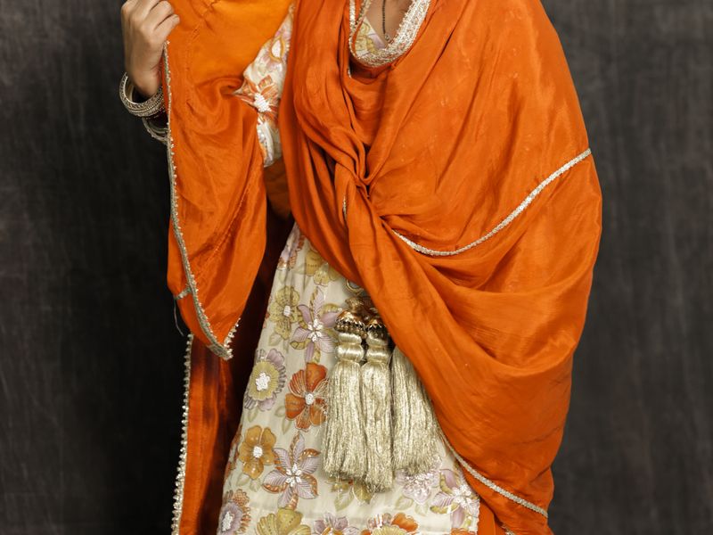 Orange silk dupatta draped over a floral sangeet outfit