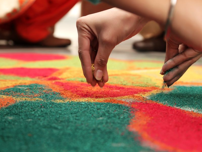 Hands sprinkling coloured powder onto a rangoli design